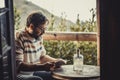 Adult bearded hipster man reading a book sitting outside at home in terrace patio enjoying relax and education concept lifestyle.