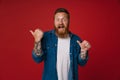 Adult bearded tattooed handsome enthusiastic redhead man pointing aside