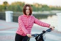 Adult beautiful redhead woman with bob haircut posing on bicycle in autumn city river pier Royalty Free Stock Photo