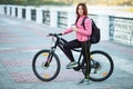 Adult beautiful redhead woman with bob haircut thinking drinking morning coffee posing on bicycle in autumn city river pier Royalty Free Stock Photo