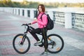 Adult beautiful redhead woman with bob haircut thinking drinking morning coffee posing on bicycle in autumn city river pier Royalty Free Stock Photo