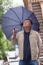 An adult blond man with an umbrella on the street looks distance waiting