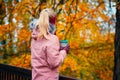 Adult blond woman holds a cup of herbal tee in hands in beautiful autumn forest golden leaves in background Royalty Free Stock Photo