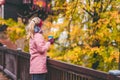 Adult blond woman holds a cup of herbal tee in hands on wooden bridge with beautiful golden autumn leaves in background Royalty Free Stock Photo