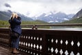 Adult blonde woman takes photos of Swiftcurrent Lake on the deck of the Many Glacier Hotel in Glacier National Park Montana USA Royalty Free Stock Photo