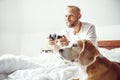 Adult breaded man waked up and plays PC games don`t stands up from bed.His beagle dog watching the game with very interest