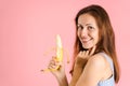 An adult brunette holds a peeled banana in her hand and smiles sexually. Studio shot on a pink background Royalty Free Stock Photo