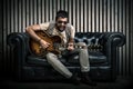 Adult caucasian guitarist portrait playing electric guitar sitting on vintage sofa. Music singer concept on couch and