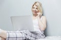 An adult Caucasian woman in her pajamas is excited to have found good news on the Internet using a laptop while making a call on a Royalty Free Stock Photo