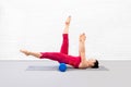 Adult caucasian woman in red sportswear lying on back and practice pilates using foam roller in fitness studio, legs and