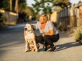 Woman caressing a dog sitting on an unpaved street