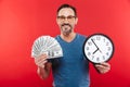 Adult cheerful positive man holding money and clock. Royalty Free Stock Photo