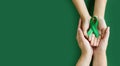 Adult and child hands holds green ribbon on green background. World lymphoma awareness day. September 15. Liver