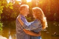 An adult couple stand on the shore of the lake in an embrace in the rays of the setting sun