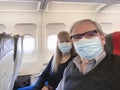 Adult couple taking a selfie while travelling by plane wearing a surgical mask during the covid pandemic Royalty Free Stock Photo