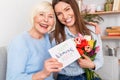 Adult daughter and her retirement mother holding postcard and tulips in hands