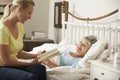 Adult Daughter Reading To Senior Female Parent In Bed At Home