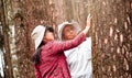 An adult daughter with senior father touching a tree in the woods. Earth`s day concept with people protecting the trees from