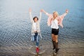 Adult daughter spending time with her mother, having fun, jumping. Mom and daughter outdoors, on walk by reservoir Royalty Free Stock Photo