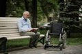 Adult disabled man with wheelchair sits on a bench