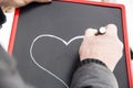 Adult draws heart on the blackboard with white marker