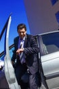 An adult, elderly, handsome man gets out of the car, looking at his watch against the background of a modern building