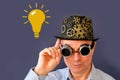 Adult elderly man in a hat and black glasses in the style of steampunk, parapunk, emotions on the face, yellow symbol light bulb,