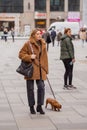 An adult fashionable elegant woman in the city hurries down the street with a dog on a leash