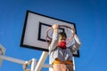 Adult female with a facemask doing chin-ups on a basketball ring in a park