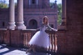Adult female Hispanic classical ballet dancer making figures leaning on a stone balustrade, wearing a white tutu