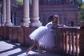 Adult female Hispanic classical ballet dancer making figures leaning on a stone balustrade, wearing a white tutu