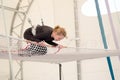 An adult female lands on a net, preparing to dismount at a on a flying trapeze school at an indoor gym. The woman is an amateur