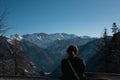 a woman standing on a ledge overlooking a mountain range and snowy trees