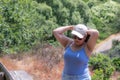 Adult female tourist putting on cap and tying her hair with it, standing on a lookout Royalty Free Stock Photo