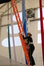 An adult female trapeze artist climbs a ladder leading up to a trapeze platform to perform a jump