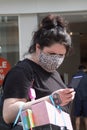Adult female wearing face mask walking along a high street with shopping bags reading on her mobile phone