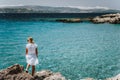 Adult female in white dress on summer vacation enjoying sea coast landscape of small beach with crystal clear blue water Royalty Free Stock Photo