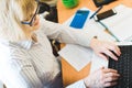 Adult focused blonde woman in glasses using laptop, writing notes in workplace at home. Remote training, learning. Female watching Royalty Free Stock Photo