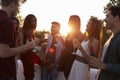 Adult friends socialising at a party on a rooftop at sunset