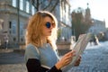 Adult girl in blue sunglassed is looking at the paper map and searching for direction early in the morning in ancient Royalty Free Stock Photo