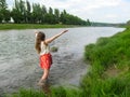 Adult girl with long blond hair splashes in the water of Uzh River - back view. A young woman enjoys spring freshness of water, Royalty Free Stock Photo