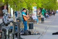 An adult gray-haired man plays guitar and sings on a city street.