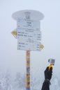 Adult hand holding a Gopro camera taking photos of the trail sign of Mount Revan on snowy foggy day