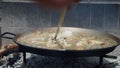 An adult hand stirs the rice in the paella pan