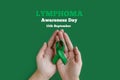 Adult hands holds green ribbon on green background. World lymphoma awareness day. September 15. Cancer and Lymphoma