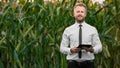 Adult, handsome, stylish, businessman holding a black, new tablet and standing in the middle of green and yellow corn field Royalty Free Stock Photo