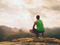 Adult hiker in black shorts and green singlet sit on mountain edge. Man enjoying view Royalty Free Stock Photo