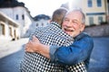 An adult hipster son and his senior father in town, hugging.