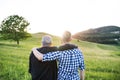 An adult hipster son with senior father standing in nature at sunset. Rear view.