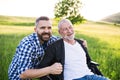 An adult hipster son with senior father in wheelchair on a walk in nature at sunset, laughing. Royalty Free Stock Photo